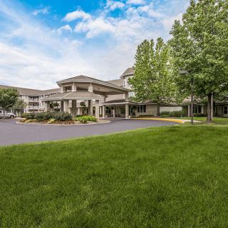 A modern building with a green lawn and trees under a blue sky with clouds.