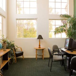 A cozy office space with computers, desks, and natural light from large windows.