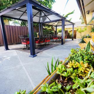 A cozy outdoor space featuring a gazebo with seating, surrounded by lush greenery.