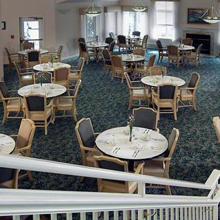 An empty dining area with round tables and chairs arranged neatly on a carpeted floor.