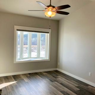 An empty room with a ceiling fan and large window, featuring hardwood floors.
