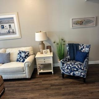 A cozy living room setup featuring a white sofa, a blue floral armchair, a lamp, and decorative elements.
