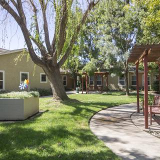 A peaceful backyard with a green lawn, trees, and patio seating under a sunny sky.