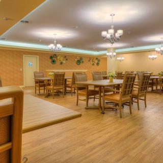 A spacious dining room with wooden floors, featuring several tables and chairs under elegant chandeliers.