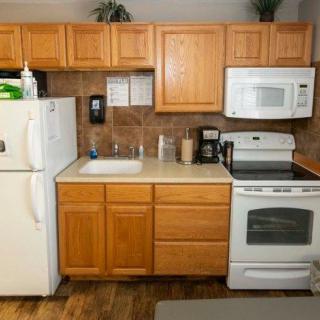 A compact kitchen featuring wooden cabinets, a microwave, oven, refrigerator, sink, and countertop.