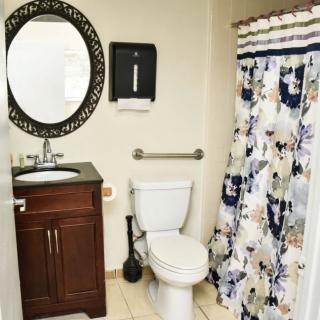 A well-organized bathroom with a round mirror, sink, toilet, and a floral shower curtain.