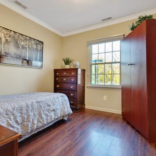 A cozy bedroom featuring a single bed, dresser, and wardrobe with natural light streaming through the window.