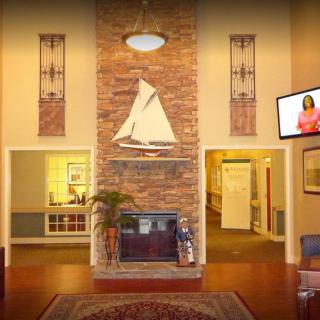 A cozy living room with a fireplace adorned by a sailboat decoration, surrounded by warm lighting and a television mounted on the wall.