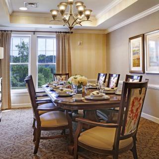 Elegant dining room with a large table set for dinner, featuring classic chairs, a chandelier, and large windows with curtains.
