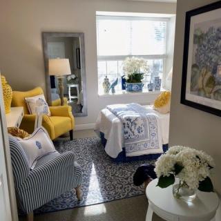 A cozy bedroom with bright yellow accents and a sunlit window, featuring a striped chair and a decorative floral arrangement.