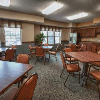 A cozy dining area with multiple tables and chairs, accompanied by a kitchenette and large windows.