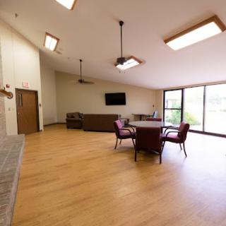 A spacious lounge with wooden flooring and ample natural light, featuring comfortable seating.