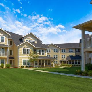 A residential apartment building with a well-maintained green lawn and a clear blue sky.