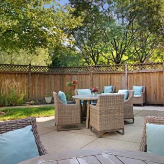 A cozy outdoor patio with wicker furniture and blue cushions surrounded by a wooden fence and lush trees.