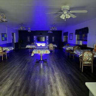 A spacious dining area illuminated with blue lighting, featuring decorative furniture and ceiling fans.