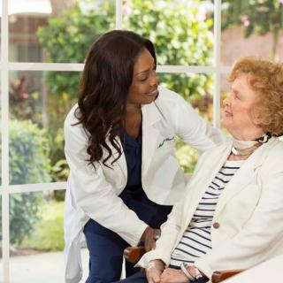 A doctor converses with an elderly patient in a bright, indoor setting.
