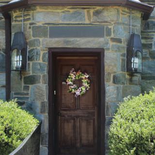 An inviting entrance featuring a wooden door adorned with a floral wreath, set against a stone wall.