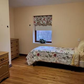 A cozy bedroom with a single bed, dresser, and window adorned with printed curtains.