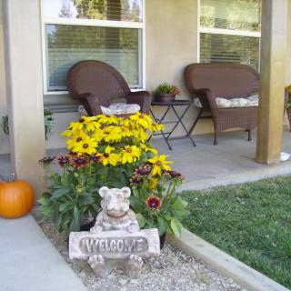 A cozy front porch with wicker chairs, vibrant yellow flowers, a pumpkin, and a welcome sign statue.