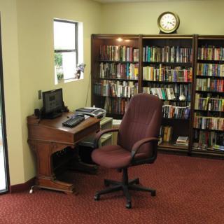 A cozy library corner featuring a desk with a computer and a comfortable chair, surrounded by bookshelves filled with books.