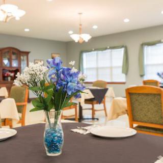 A dining room with a table set and a vase of colorful flowers.