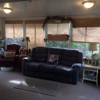 A cozy living room featuring a sofa, armchair, and large windows with blinds.