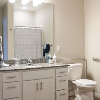A modern bathroom featuring a spacious vanity with granite countertops, a toilet, and a shower curtain.