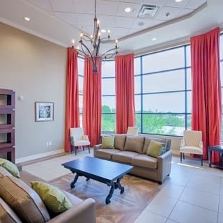 A modern living room with spacious seating, featuring a chandelier and large windows adorned with red curtains.