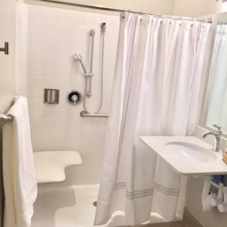 An accessible bathroom with a shower chair, grab bars, and a sink.
