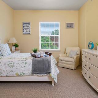 A cozy bedroom with a bed, chair, and dresser, featuring soft lighting and decor.