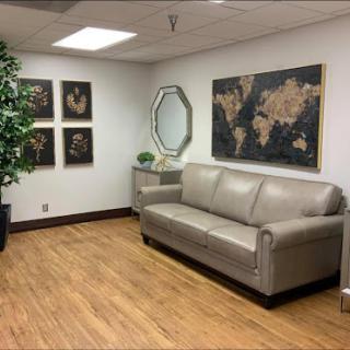 A cozy office waiting area featuring a comfortable sofa, decorative artwork, and greenery.