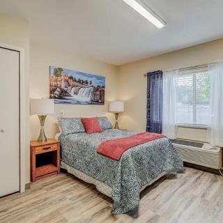 A cozy bedroom with a colorful bedspread, two lamps on nightstands, and a large window allowing natural light in.