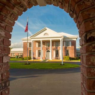 A colonial-style building framed by a brick archway, featuring white pillars and an American flag in the foreground.