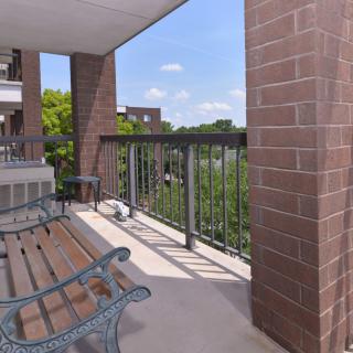 A cozy apartment balcony with outdoor seating and a view of the trees.