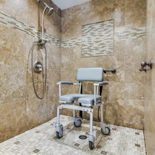 An accessible walk-in shower with a rolling shower chair and decorative tiles.