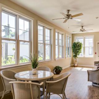 A bright sunroom featuring large windows, a dining set, and ceiling fans.