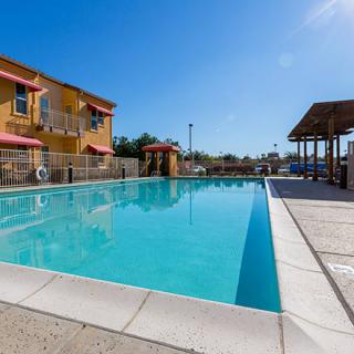 A serene outdoor swimming pool next to a residential or resort building under a clear blue sky.