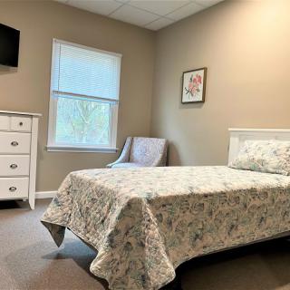 A cozy bedroom with a single bed, dresser, chair, and television.