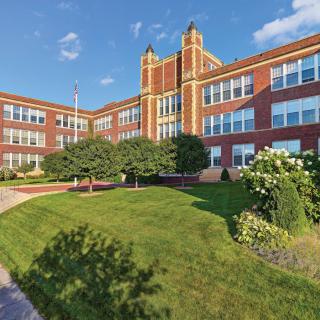 A classic brick school building with a well-maintained lawn and clear blue sky.