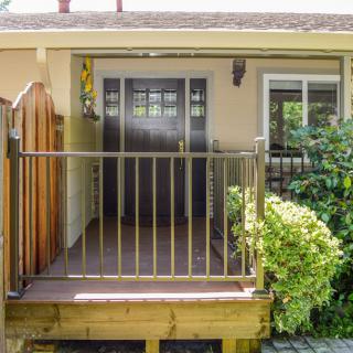 A small porch with railings and a sliding glass door leading to the interior of a house, surrounded by greenery.