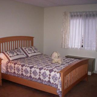 A neatly arranged bedroom featuring a wooden bed with a patterned quilt and pillows, next to a window with curtains.