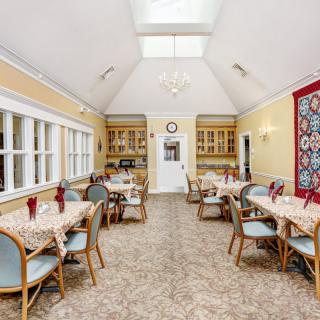 A well-lit dining room with several tables and chairs, featuring large windows and a skylight.