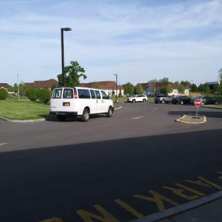 A white van parked in a parking lot surrounded by greenery.