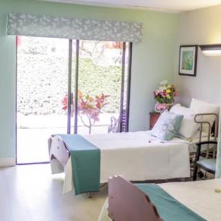 A cozy bedroom with two beds, adorned with floral arrangements and a large window offering natural light.