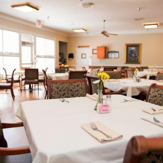 A well-lit dining room with elegantly set tables and chairs, ready for service.