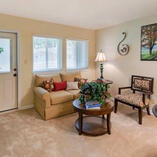 A cozy living room featuring a sofa, chair, and coffee table with a lamp and decorations against a neutral backdrop.
