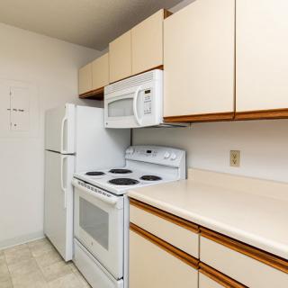 A compact kitchen with a refrigerator, stove, microwave, and wooden cabinets.