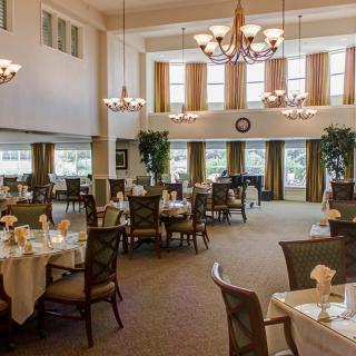 An elegant dining area with multiple round tables, chandeliers, and large windows.