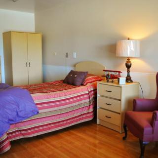 A cozy bedroom with a bed, nightstand, lamp, wardrobe, and chair.