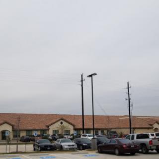 A view of a parking lot in front of a row of buildings under a cloudy sky.